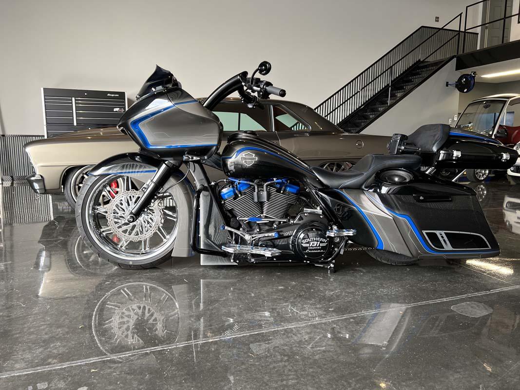 A motorcycle parked in a garage with a car in the background.